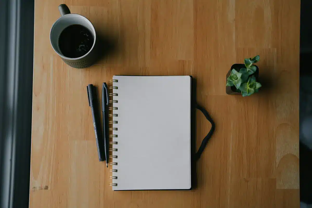 Cuaderno abierto junto a dos bolígrafos sobre una mesa de madera