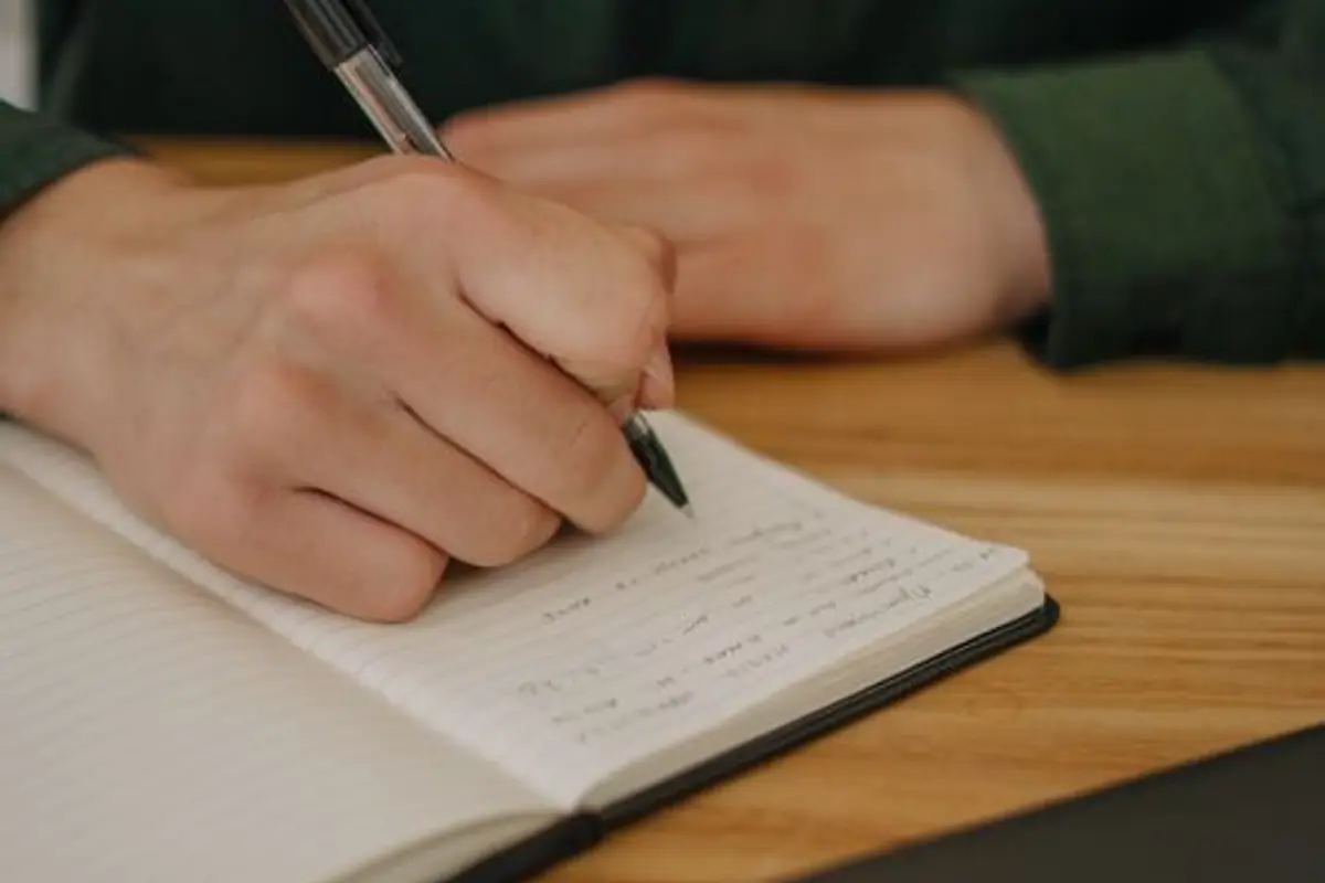 Mano escribiendo en un cuaderno sobre una mesa